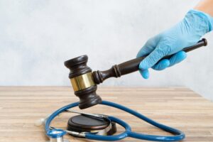 Gloved hand striking a gavel over a stethoscope, symbolizing legal judgment in medical malpractice cases