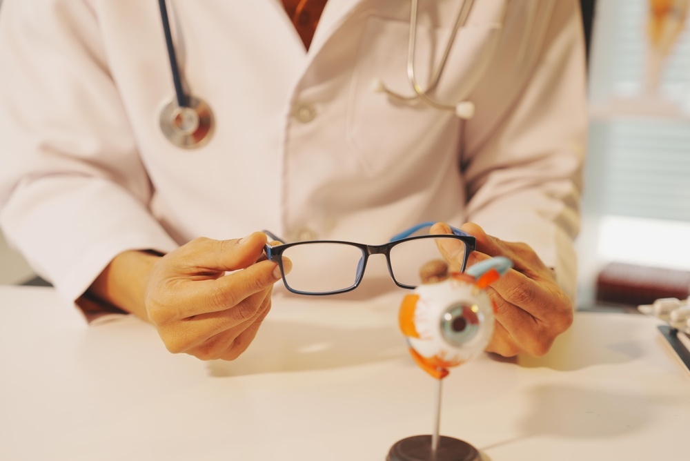 Doctor holding eyeglasses beside an anatomical eye model during an examination