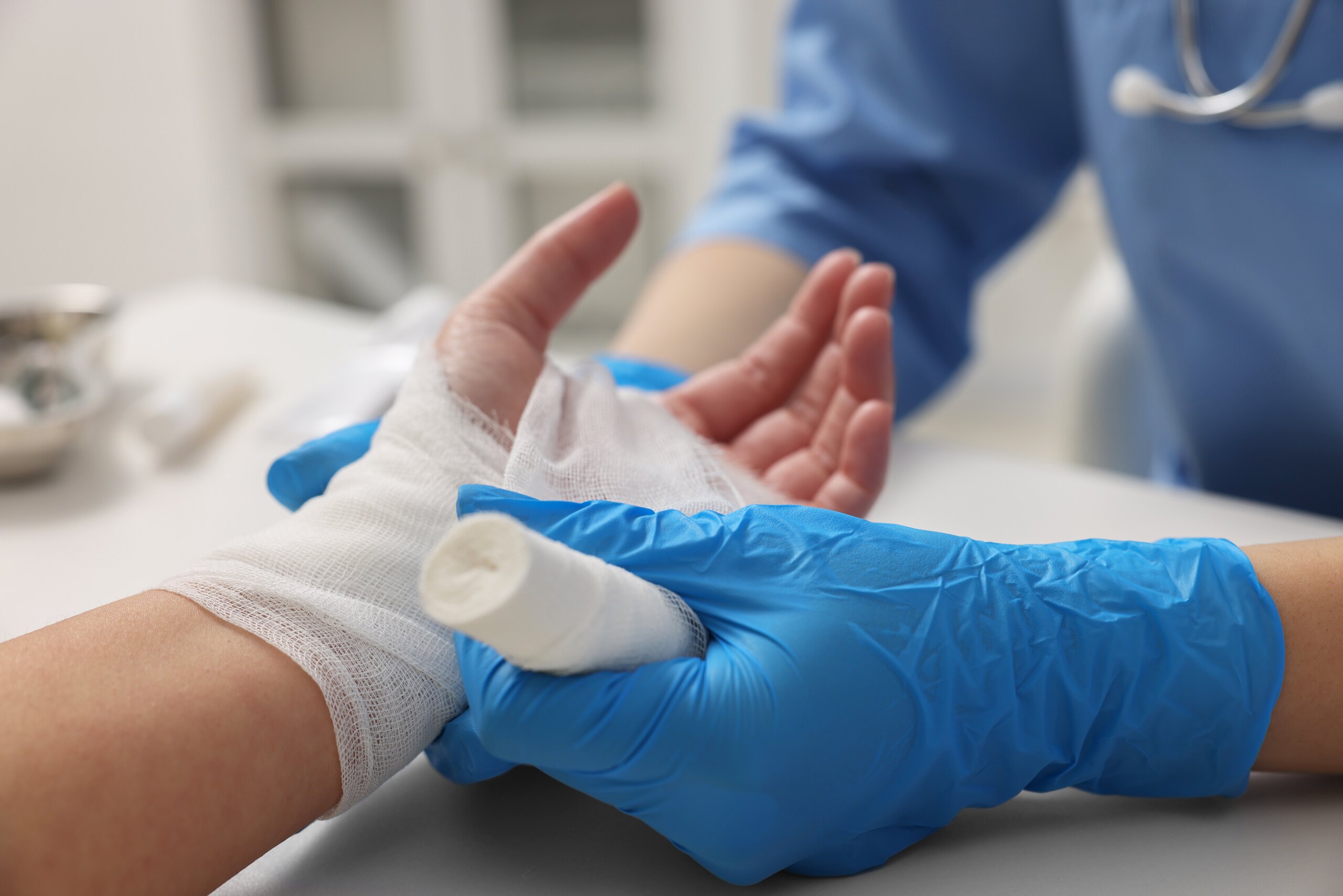 A medical professional wearing blue gloves wraps white gauze bandages around a patient's injured hand and wrist, showing the clinical treatment of damages evaluated by Tulsa burn injury attorneys.