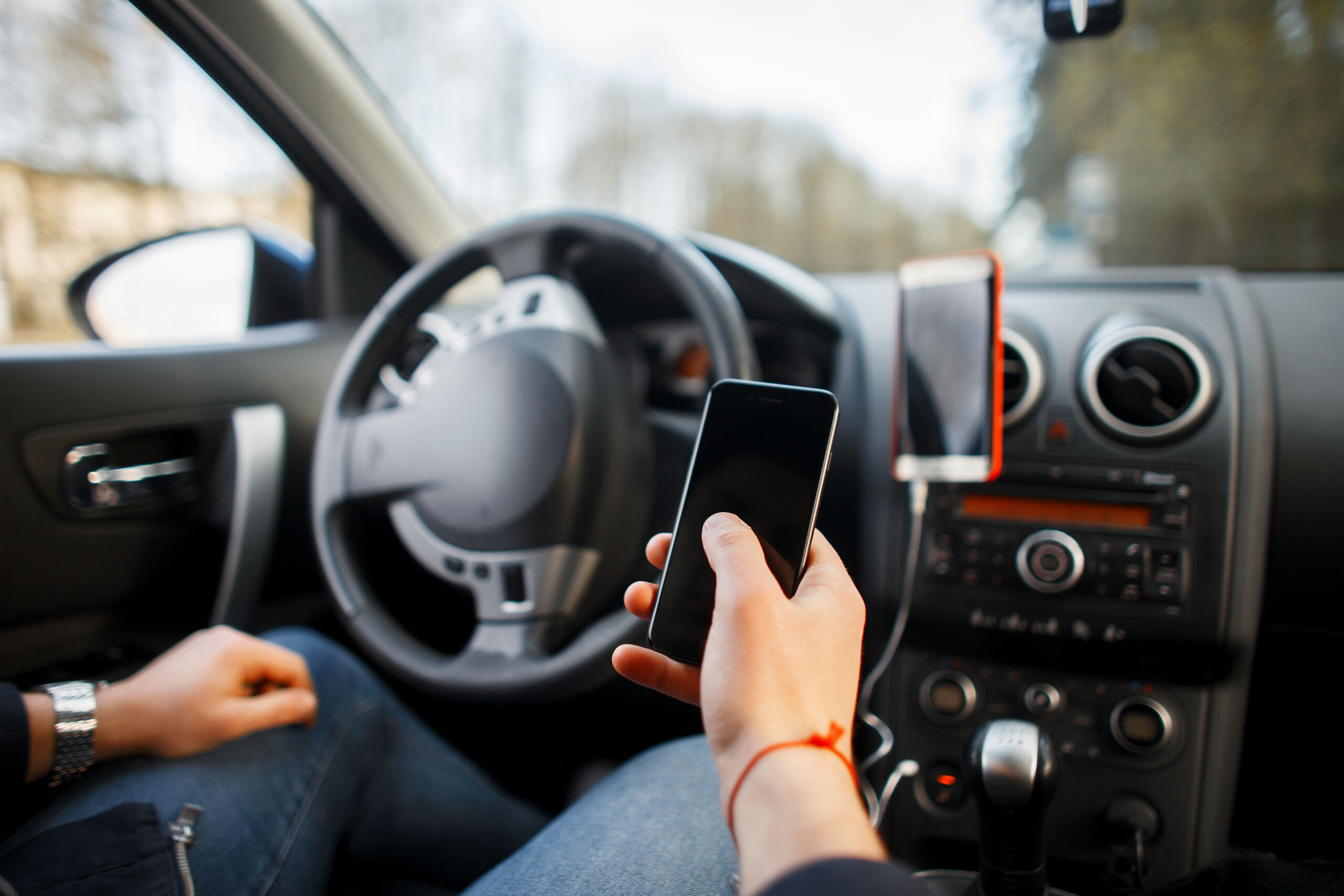 A close-up view from inside a car of a person using a smartphone while driving, demonstrating negligent behaviors investigated by Tulsa distracted driving accident lawyers.