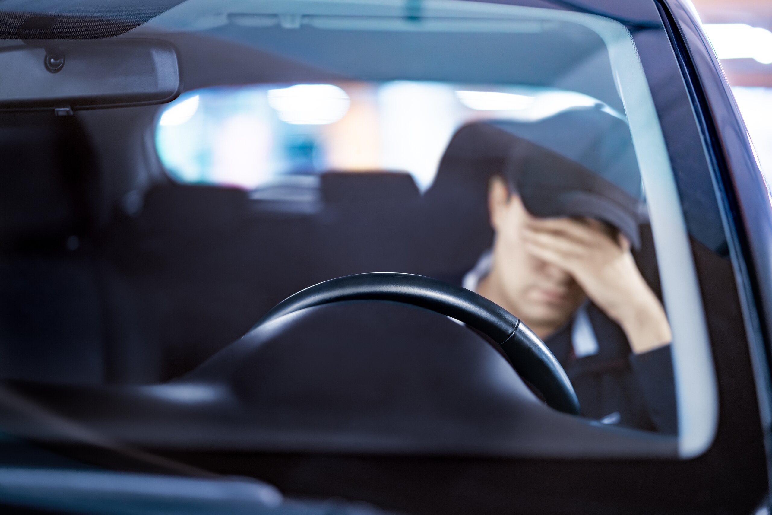 A view through a car windshield showing a stressed driver covering their face with their hand behind the steering wheel, representing the aftermath of a crash handled by Tulsa distracted driving accident lawyers.