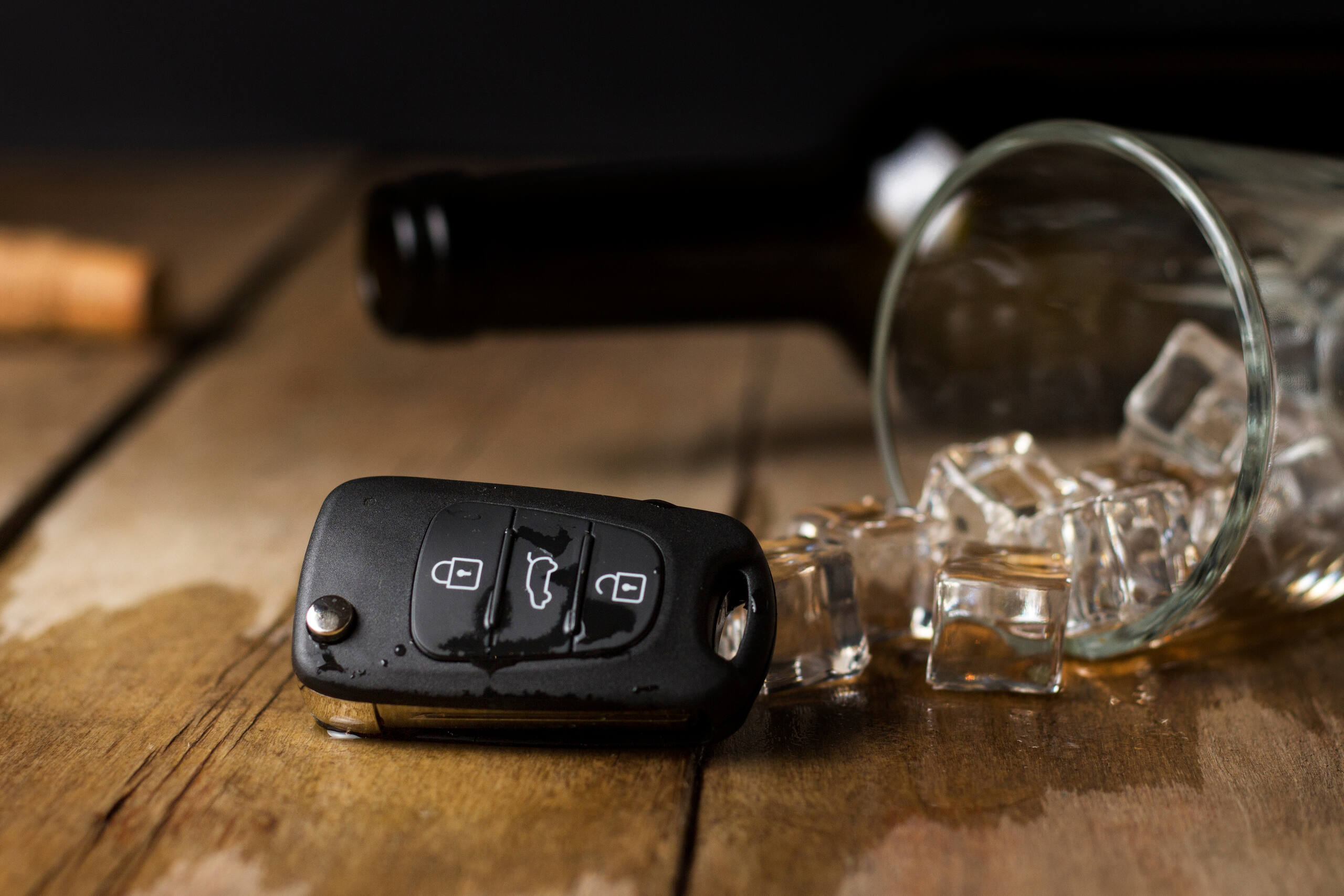 A set of car keys lying next to a spilled glass of ice on a wooden table, representing the consequences of illegal alcohol service in Tulsa.