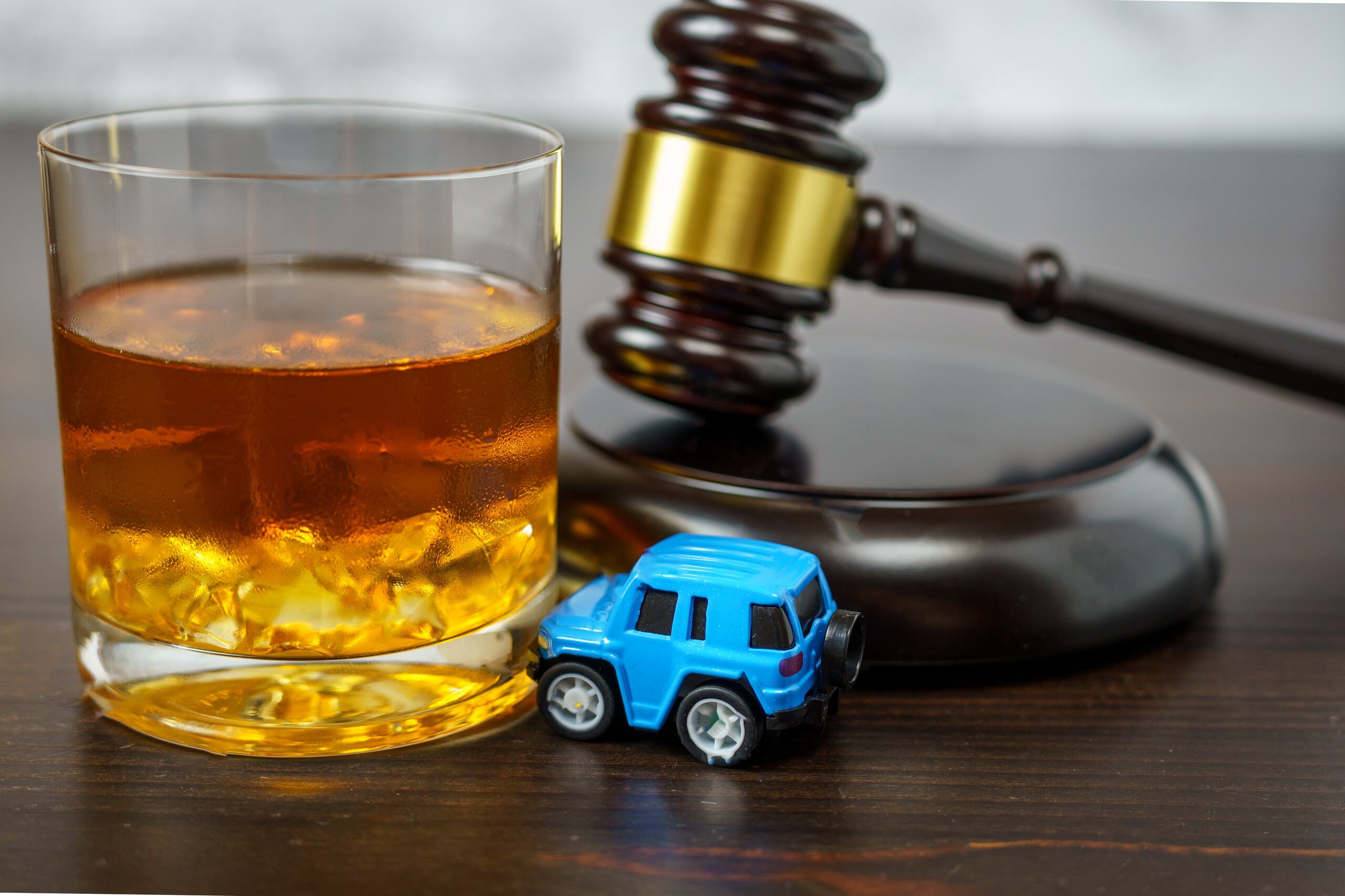 A glass of liquor next to a small blue toy car and a legal gavel, illustrating Tulsa dram shop lawsuits against bars and retailers.