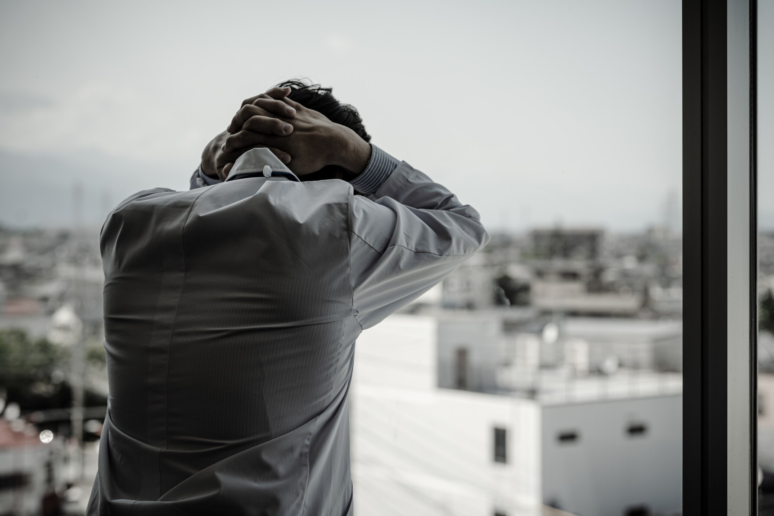 A physician in a white coat looking out a window with their hands on their head, illustrating the gravity of a wrong or delayed diagnosis in Tulsa malpractice cases.