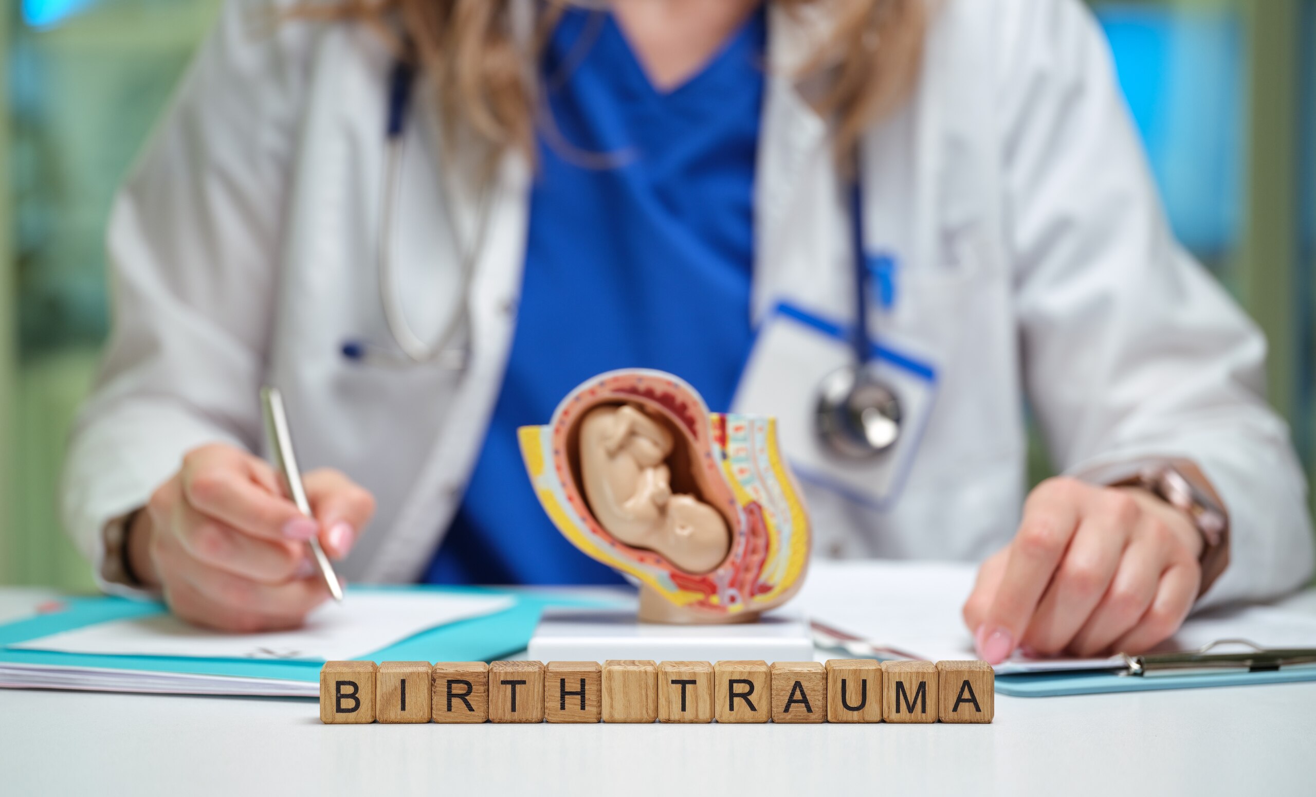 Doctor writing near a fetus model and wooden blocks spelling birth trauma for Tulsa birth injury attorneys.
