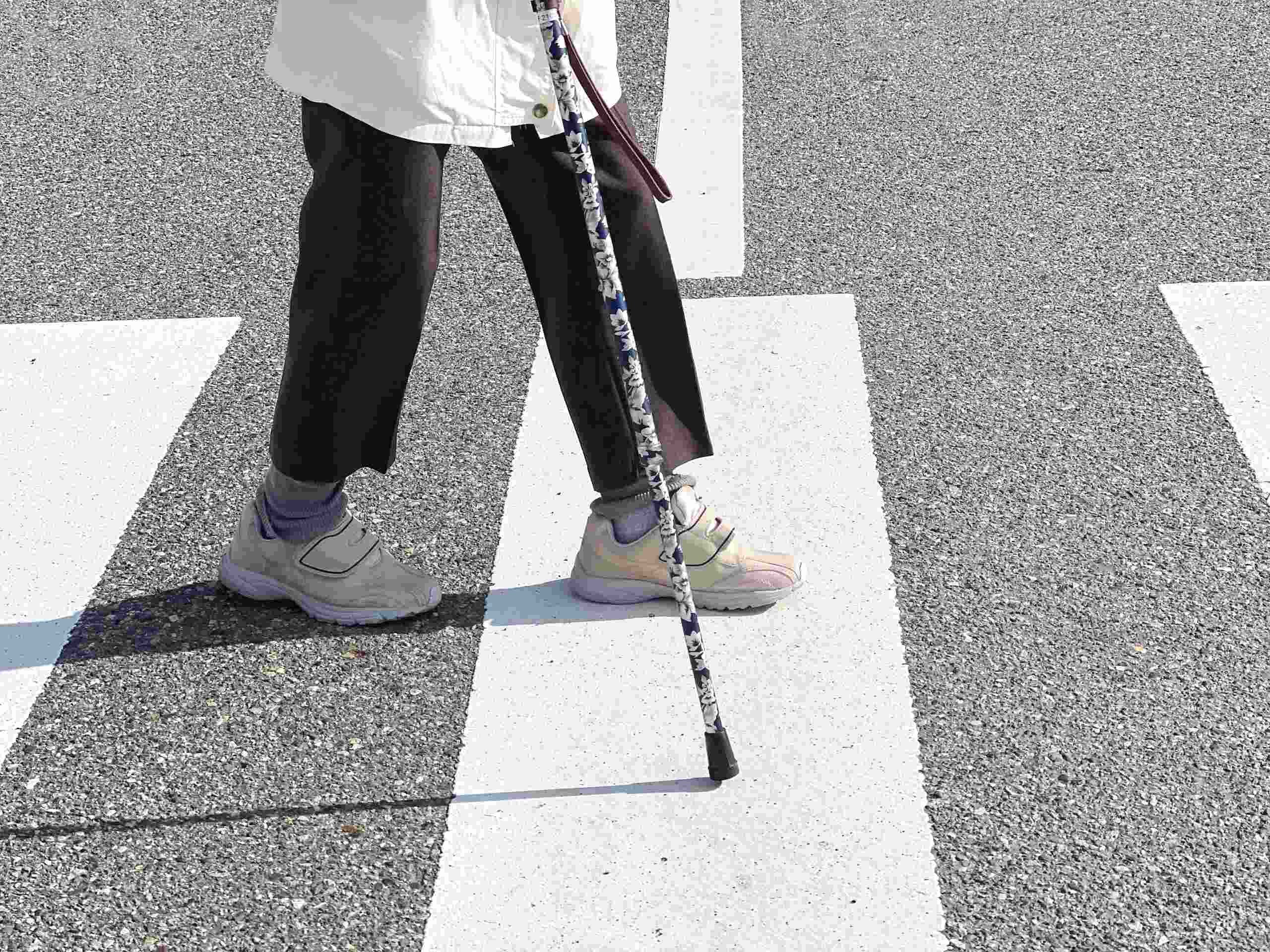 Pedestrian using a cane crossing a marked crosswalk, highlighting safety concerns after a pedestrian accident in Tulsa