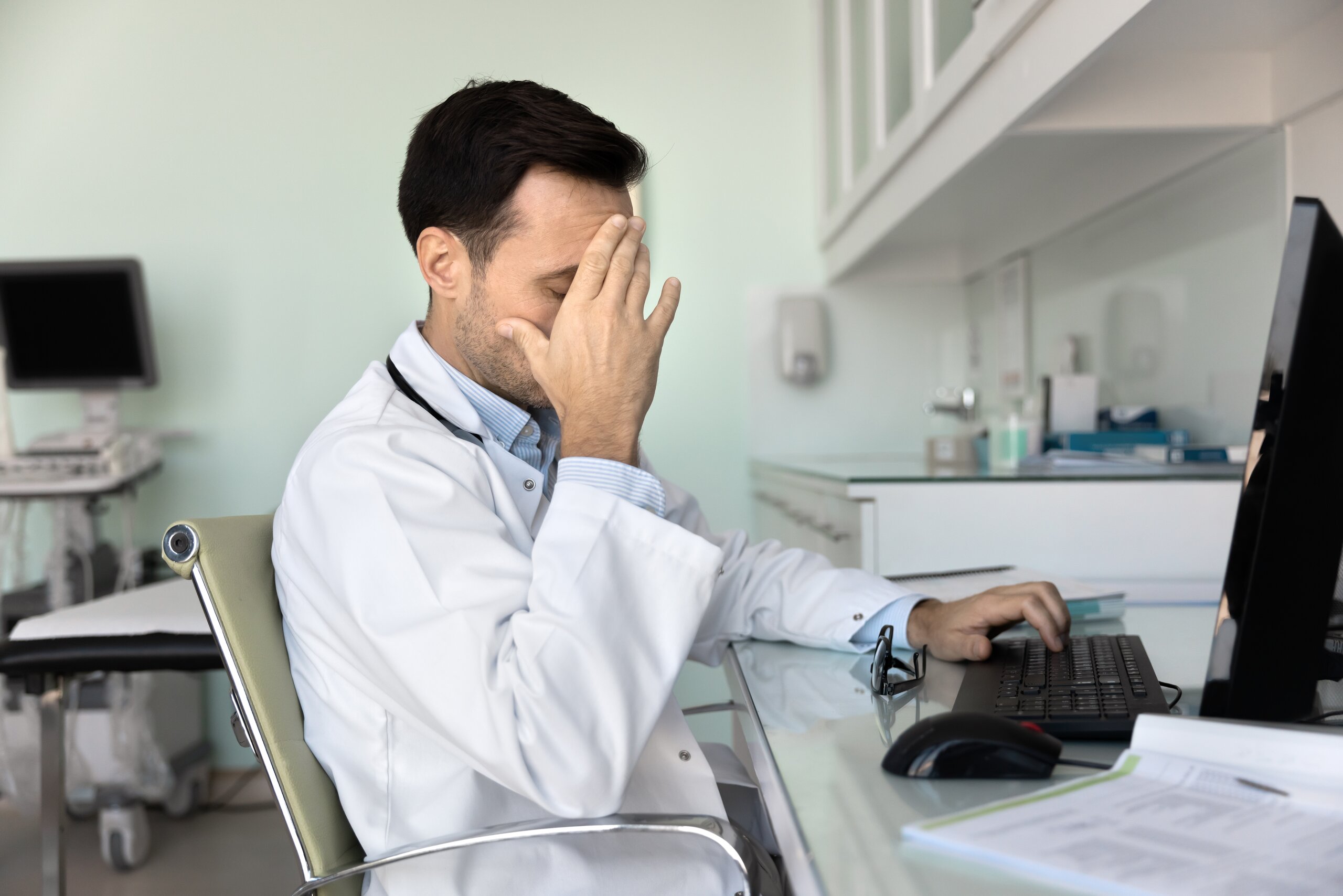 A healthcare professional appearing frustrated while reviewing medical data on a computer, representing diagnostic errors like misdiagnosis or failure to diagnose.