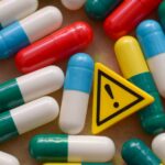 A yellow warning triangle icon surrounded by colorful medication capsules, symbolizing the risks and legal damages associated with dangerous drugs in Oklahoma.