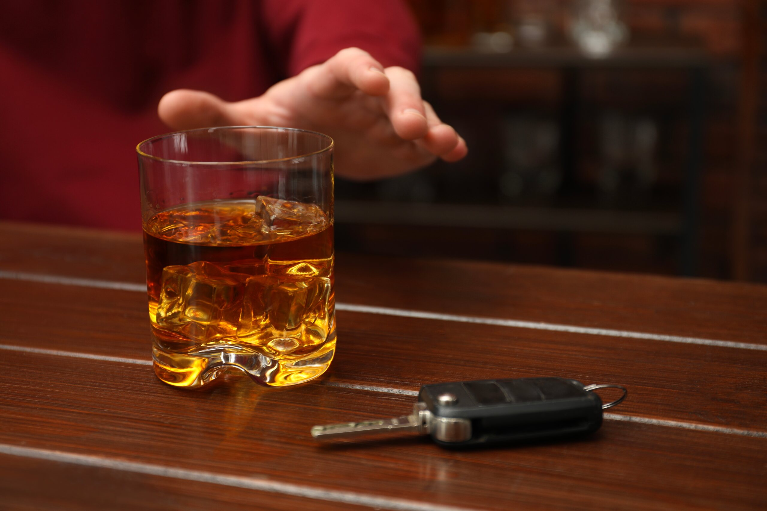 A hand reaching for a glass of whiskey next to car keys, illustrating Oklahoma dram shop laws and the legal responsibility of bars in drunk driving cases.