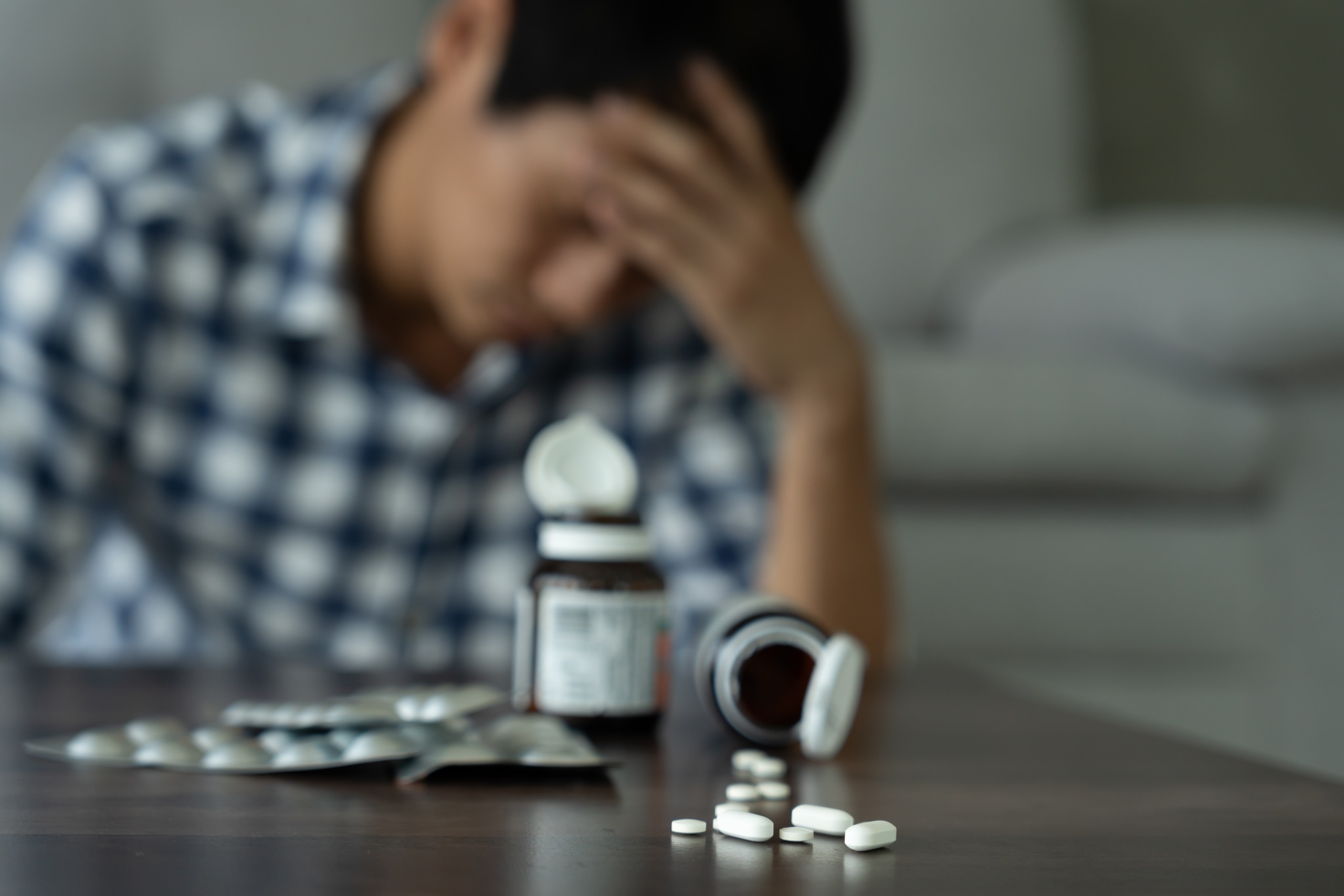 A person in Tulsa appearing unwell with prescription bottles and pills on a table.