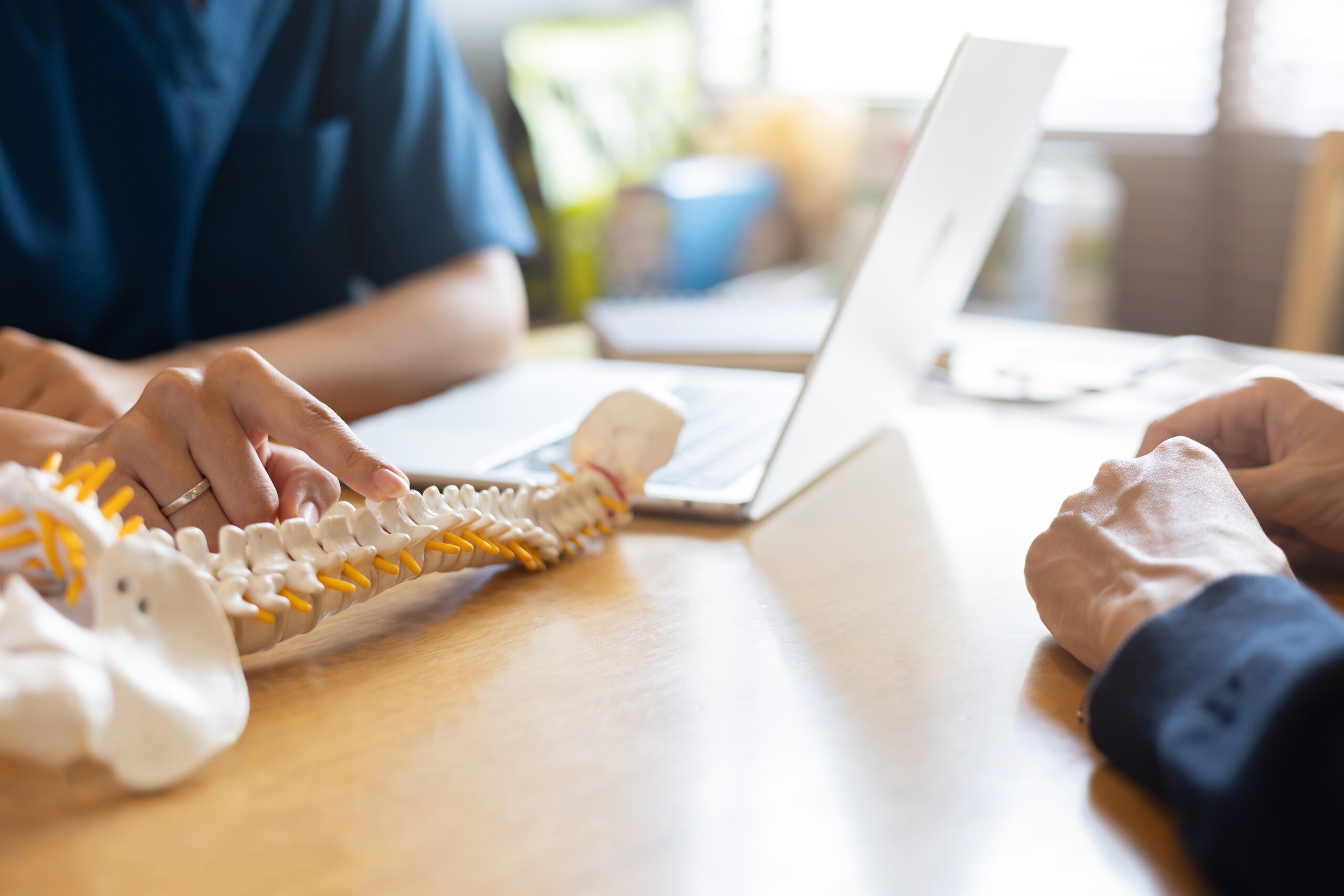 A medical professional points to a plastic anatomical model of a human spine on a desk during a consultation with a patient, demonstrating the assessment of paraplegia vs. quadriplegia in Oklahoma injury claims.