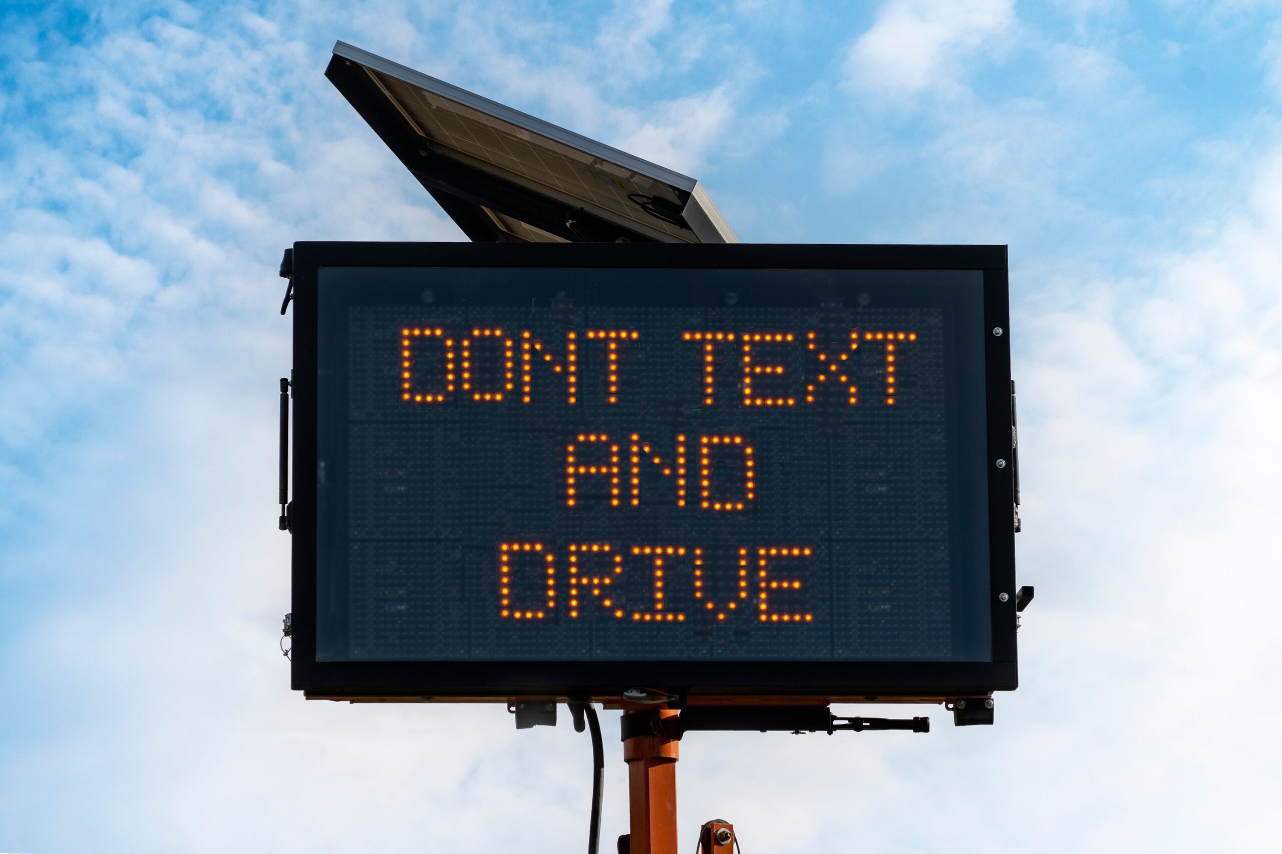 An outdoor digital road safety sign displays the warning message "DONT TEXT AND DRIVE" in orange lights against a cloudy blue sky, highlighting issues involving distracted driving punitive damages OKC.