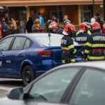 Firefighters in red helmets inspect a blue car with an Uber decal on the door at a traffic accident scene, illustrating situations involving wrongful death after an Uber or Lyft accident in Oklahoma.