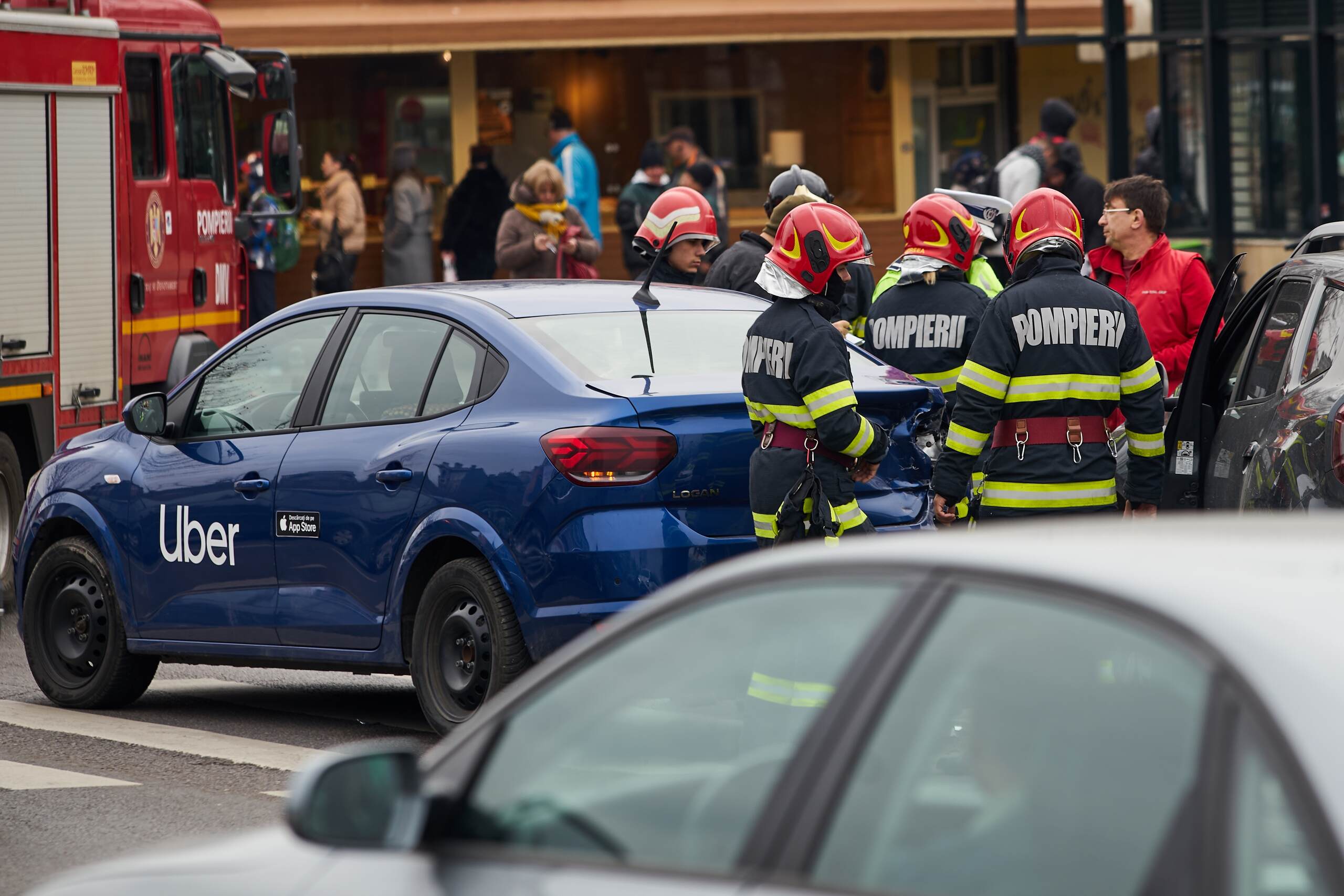 Firefighters in red helmets inspect a blue car with an Uber decal on the door at a traffic accident scene, illustrating situations involving wrongful death after an Uber or Lyft accident in Oklahoma.