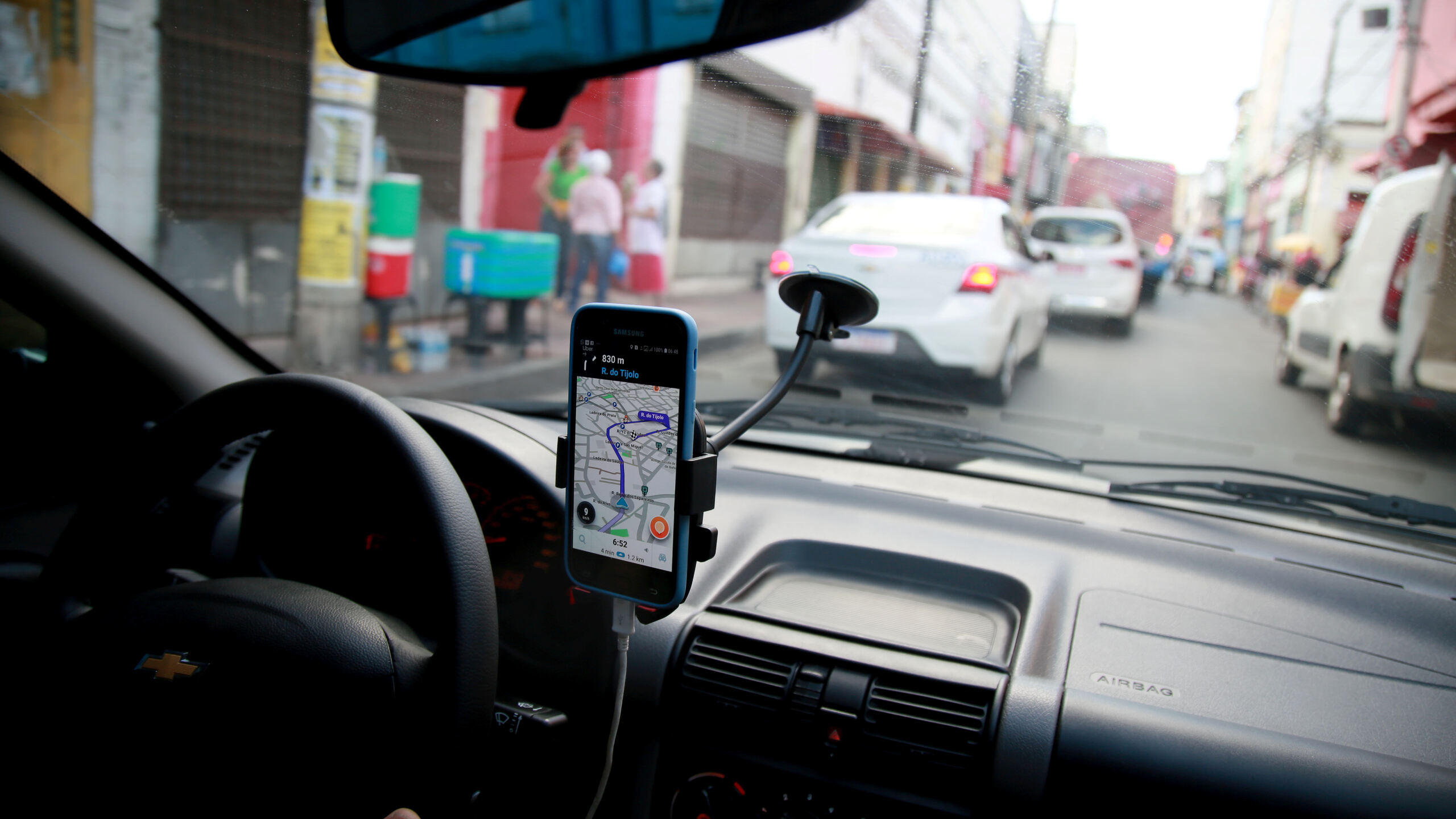 A view from inside a vehicle showing a smartphone mounted on the dashboard displaying a GPS navigation map while driving through city traffic, representing rideshare driver tracking related to wrongful death after an Uber or Lyft accident in Oklahoma.