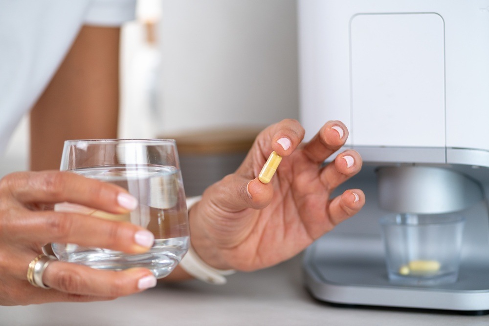 Person holding a capsule with a glass of water beside an automated pill dispenser