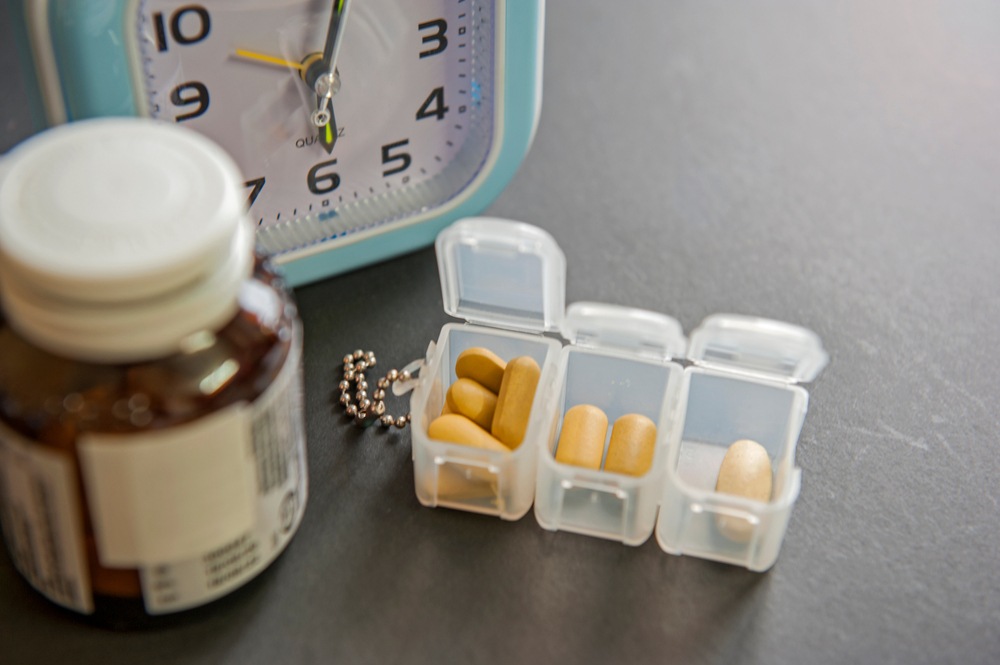 Pill organizer beside a clock and medication bottle, representing dosage timing and tracking