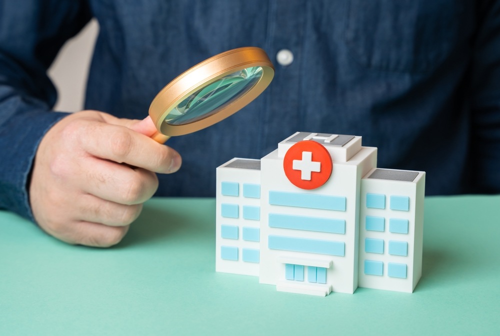 Magnifying glass examining a hospital building model, representing investigation into hospital negligence