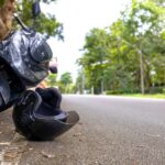 A black helmet rests on the asphalt beside a fallen scooter as riders review Oklahoma motorcycle helmet laws and how they affect your injury claim.