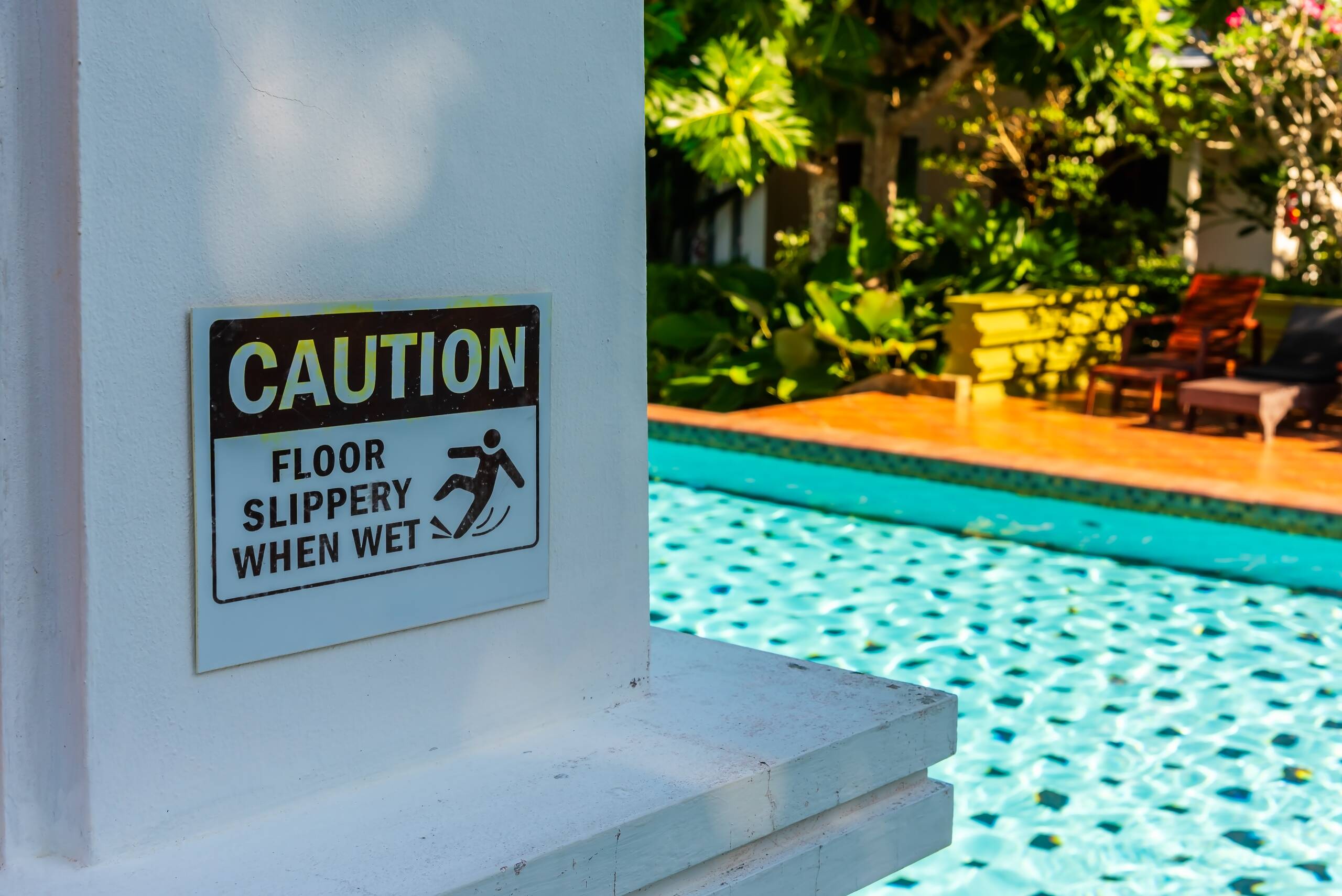 Caution slippery floor warning sign next to a resort swimming pool for Tulsa swimming pool accident attorneys.