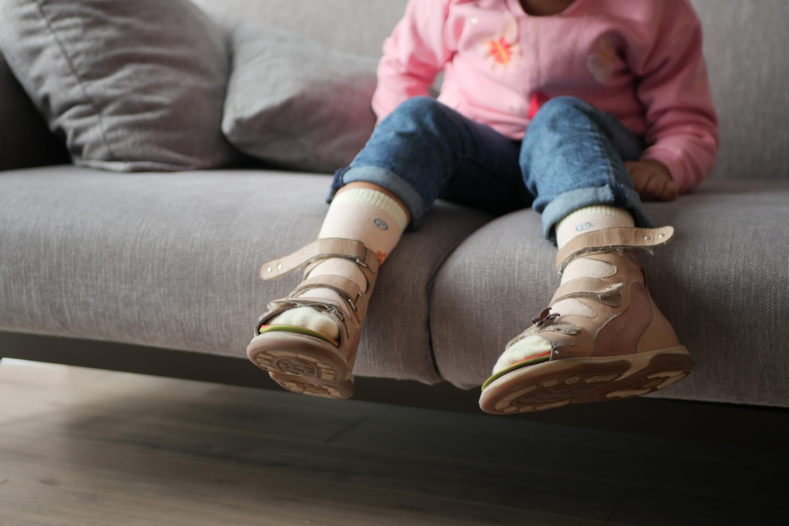 Child wearing supportive orthopedic leg braces sitting on a couch.